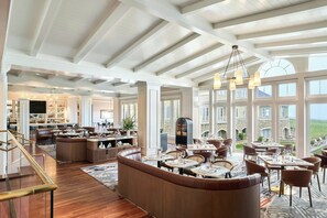Un hall d’hôtel spacieux, doté d’un haut plafond, de grandes fenêtres et d’un espace salon central.