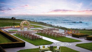 An outdoor wedding venue with a sea view, arranged seating, and a decorative arch. - The Ritz-Carlton, Half Moon Bay (Half Moon Bay)