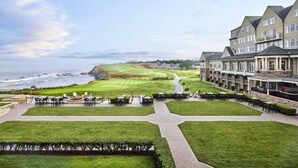 A golf course with a view of the ocean, a clubhouse with outdoor seating, and a large building with multiple windows. - The Ritz-Carlton, Half Moon Bay (Half Moon Bay)