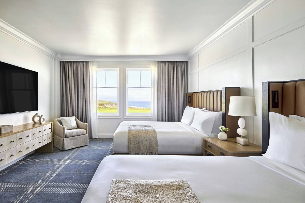 A hotel room with two beds, a TV, a desk, and a view of the outdoors.