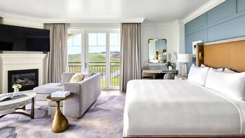 A hotel room with a large bed, a sofa, a fireplace, a television, and a view of the outdoors.