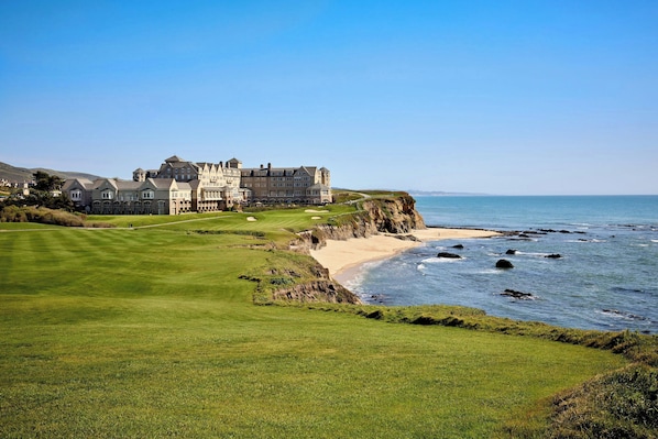 Un grand bâtiment historique, doté d’une pelouse bien entretenue et d’un terrain de golf en premier plan.