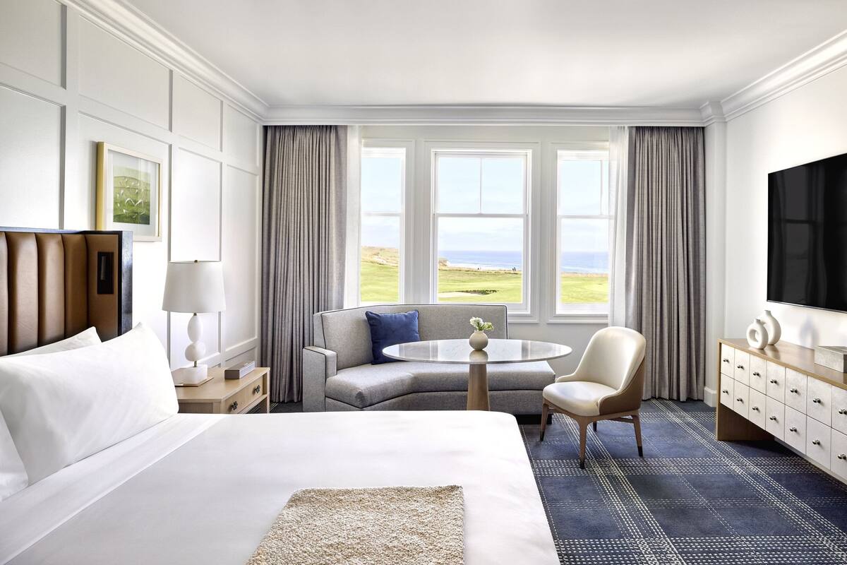 A hotel room with a large bed, a sofa, a round table, and a TV.