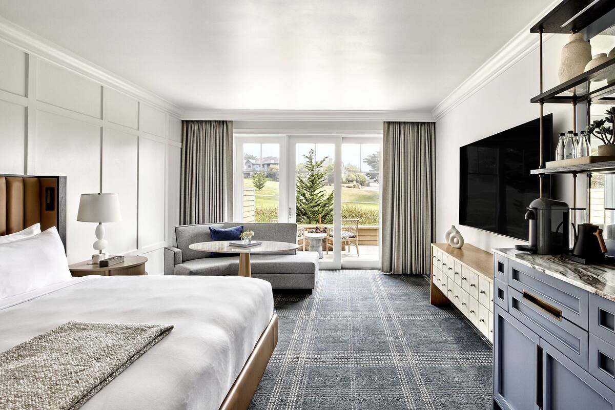 A hotel room with a large bed, a sofa, a TV, a coffee maker, and a view of the outdoors.
