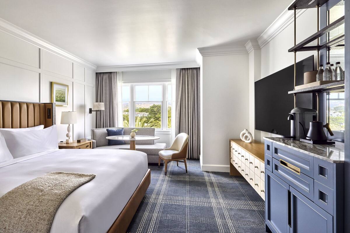 A hotel room with a large bed, a desk with a chair, a television, and a minibar.