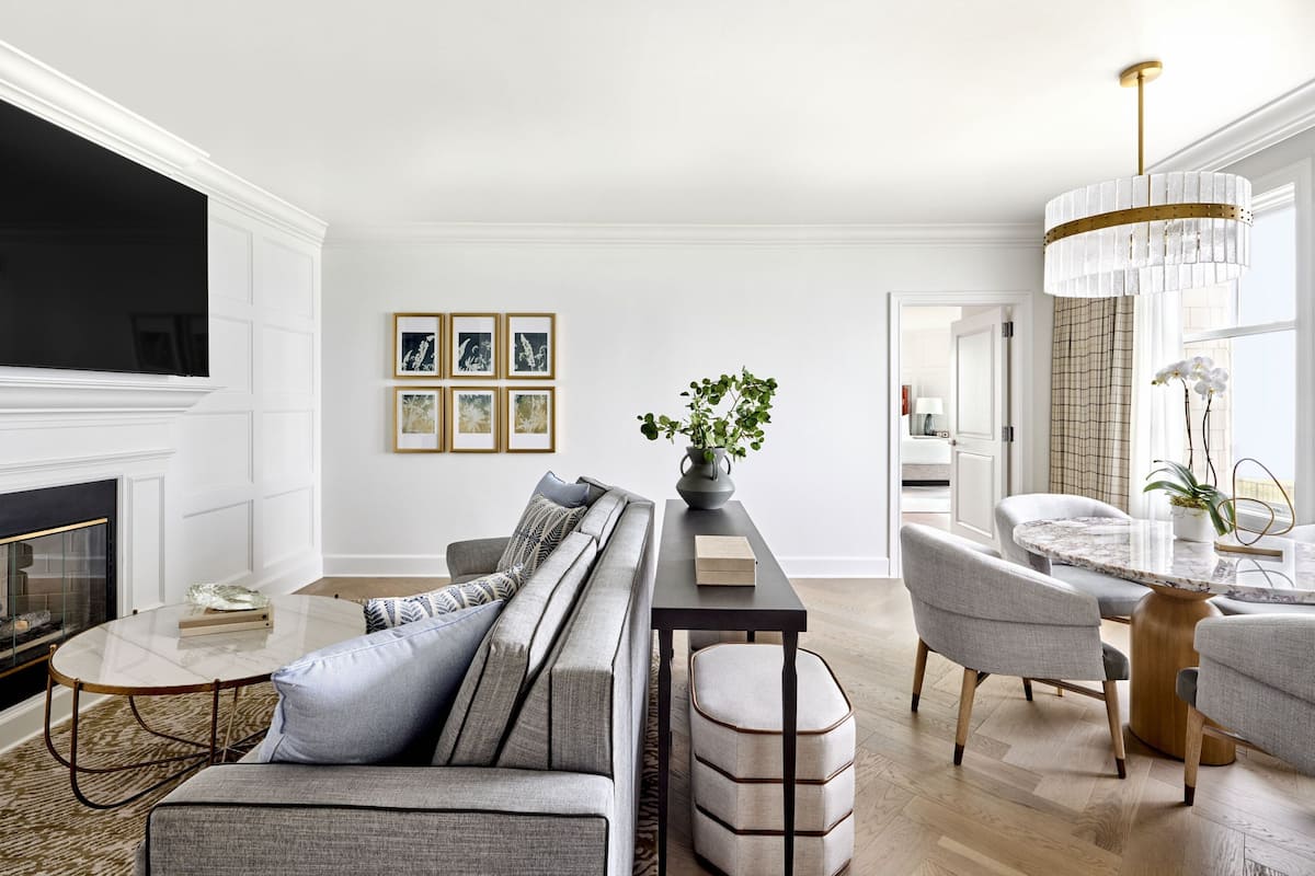 A modern living room with a fireplace, a sofa, a coffee table, and a dining area with chairs and a chandelier.
