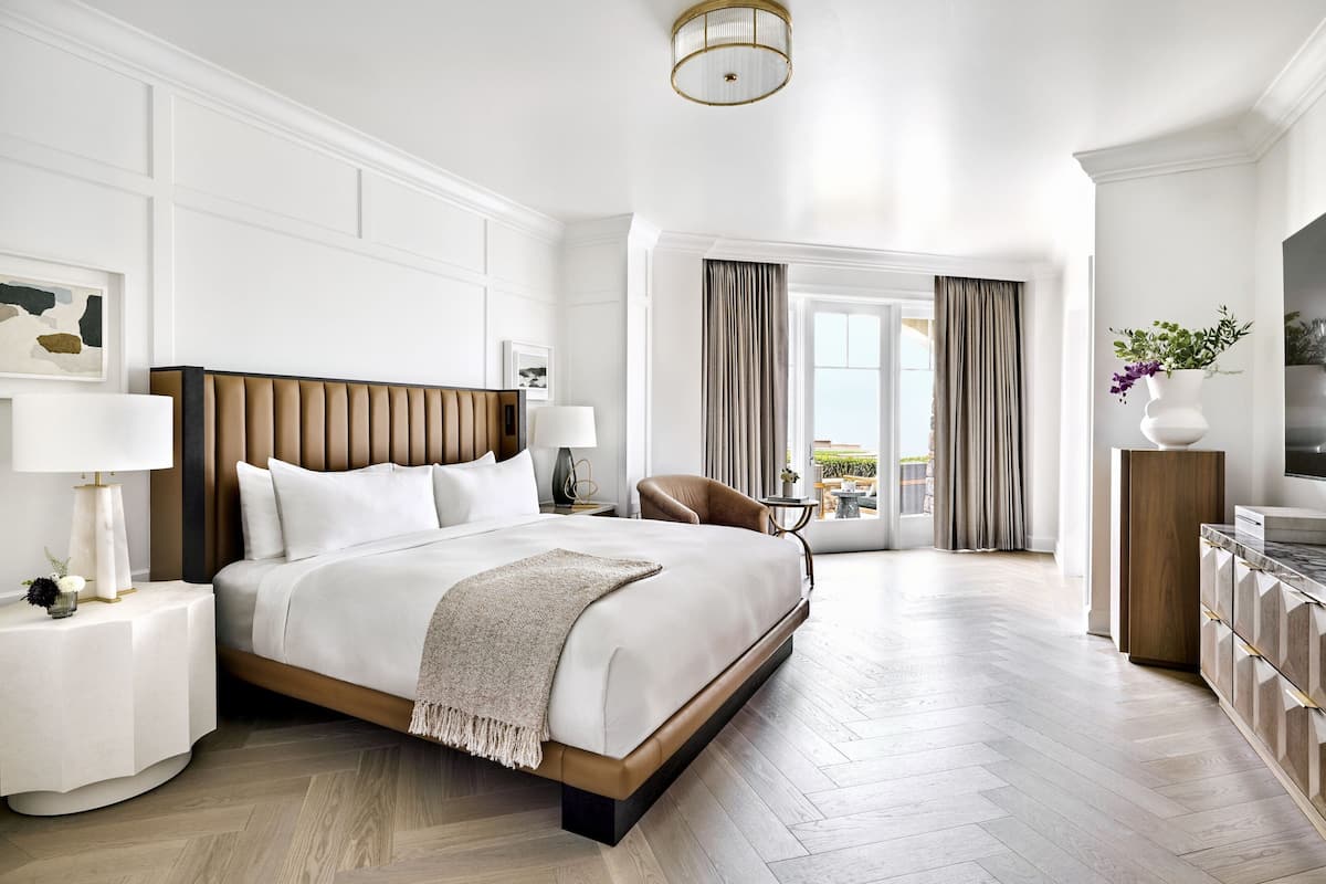 A modern hotel room with a large bed, a nightstand, a chair, and a view of the outdoors.