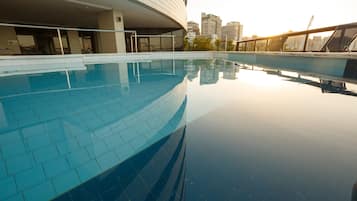Um edifício moderno com fachada de vidro curva e área de piscina com piso em azulejo.