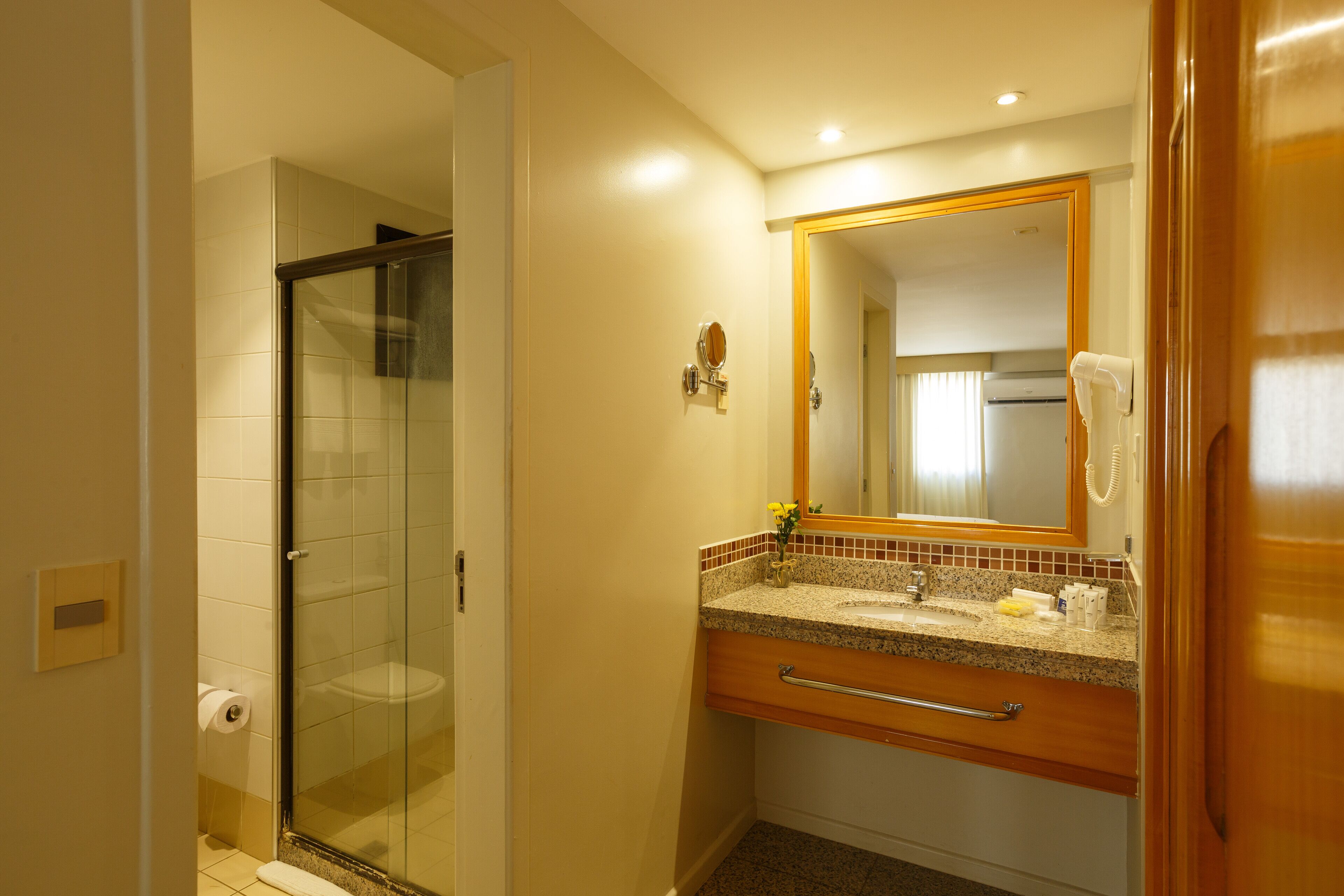 A bathroom with a glass shower enclosure, a sink with a vanity, and a mirror with a telephone.