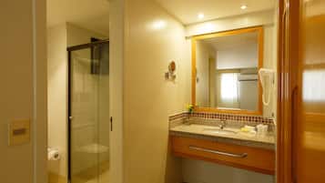 A bathroom with a glass shower enclosure, a sink with a vanity, and a mirror with a telephone.