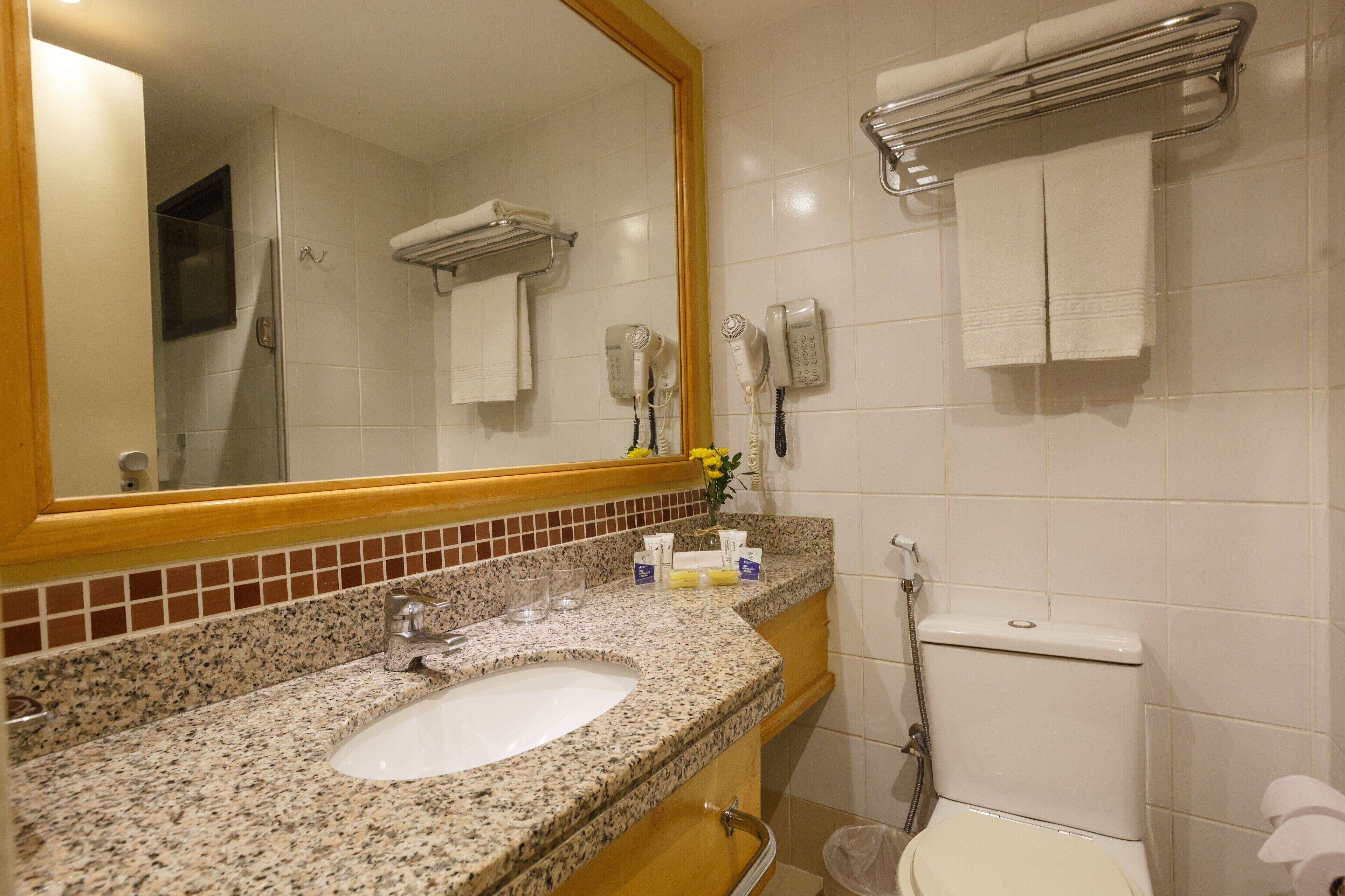A bathroom with a granite countertop sink, a mirror, a toilet, and a towel rack.