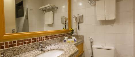 A bathroom with a granite countertop sink, a mirror, a toilet, and a towel rack.