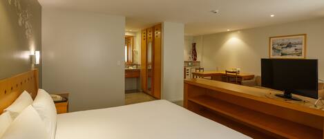 A hotel room with a large bed, a desk with a television, and a bathroom visible through an open door.