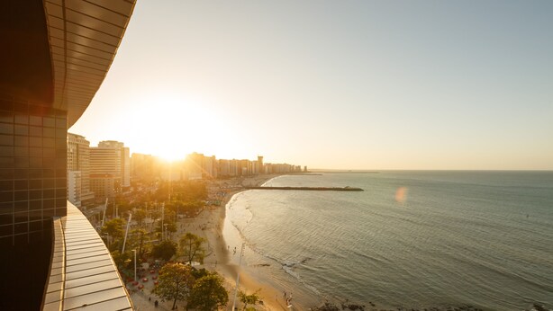 Paisagem costeira urbana com praia, edifícios e céu claro.