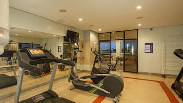 Un gimnasio con cintas de correr, elípticas y un espejo grande.