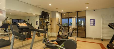 Un gimnasio con cintas de correr, elípticas y un espejo grande.