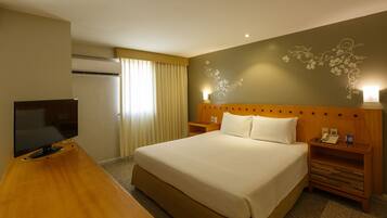 A hotel room with a large bed, a TV on a wooden desk, a nightstand with a phone, and a decorative wall piece.