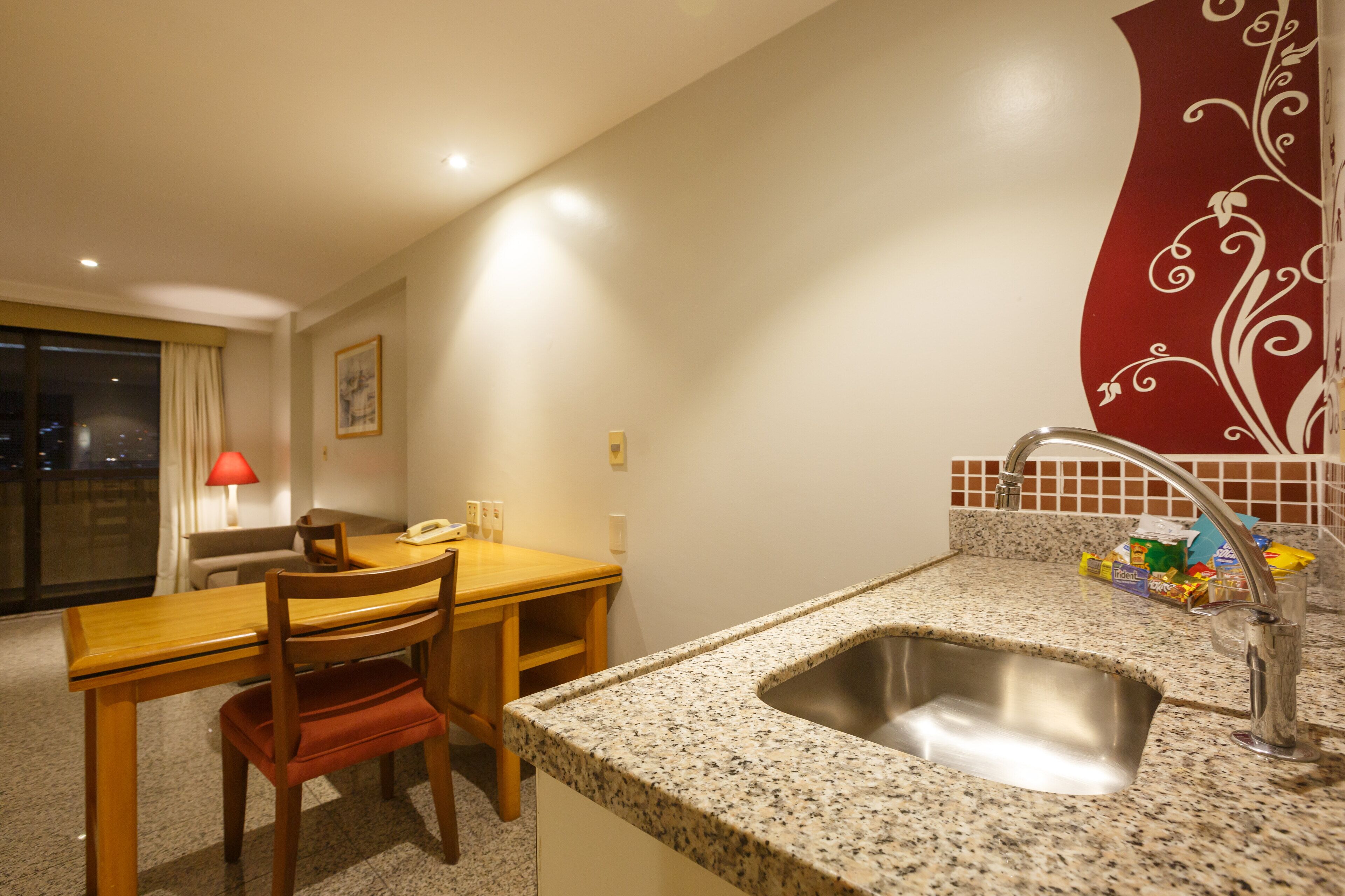 A compact kitchen with a granite countertop, stainless steel sink, and a dining area with a wooden table and chairs.