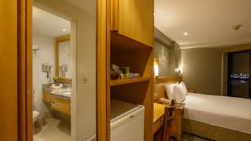 Habitación de hotel con una cama, una mesita de noche de madera, un baño con inodoro y lavamanos.