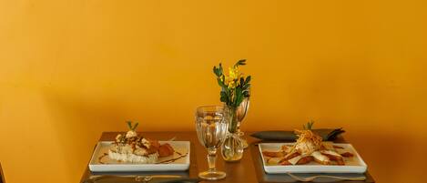 Una mesa de comedor con dos platos de comida, un florero con flores y un cuadro enmarcado de peces en la pared.