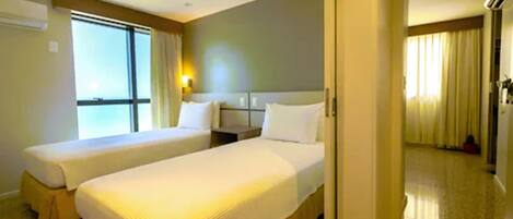 A hotel room with two single beds, a large window, a bedside table, and a nightstand.