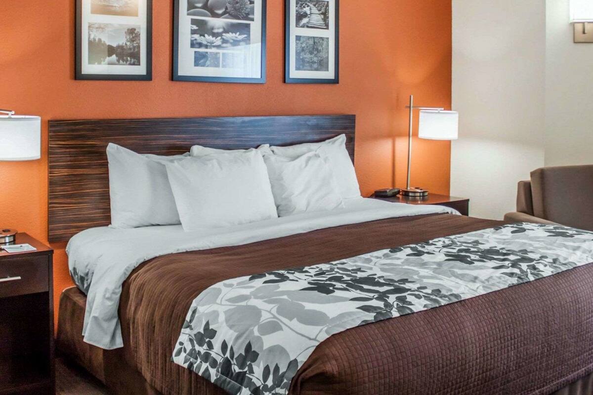 A hotel room with a large bed, two bedside tables, a nightstand, and a chair. There are three framed pictures on the wall above the bed.