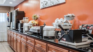 A hotel kitchen with a long counter, various appliances, and a wall-mounted artwork. - Sleep Inn North Charleston Ashley Phosphate (North Charleston)
