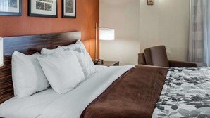 A hotel room with a neatly made bed, a chair, a lamp, and framed pictures on the wall. - Sleep Inn North Charleston Ashley Phosphate (North Charleston)