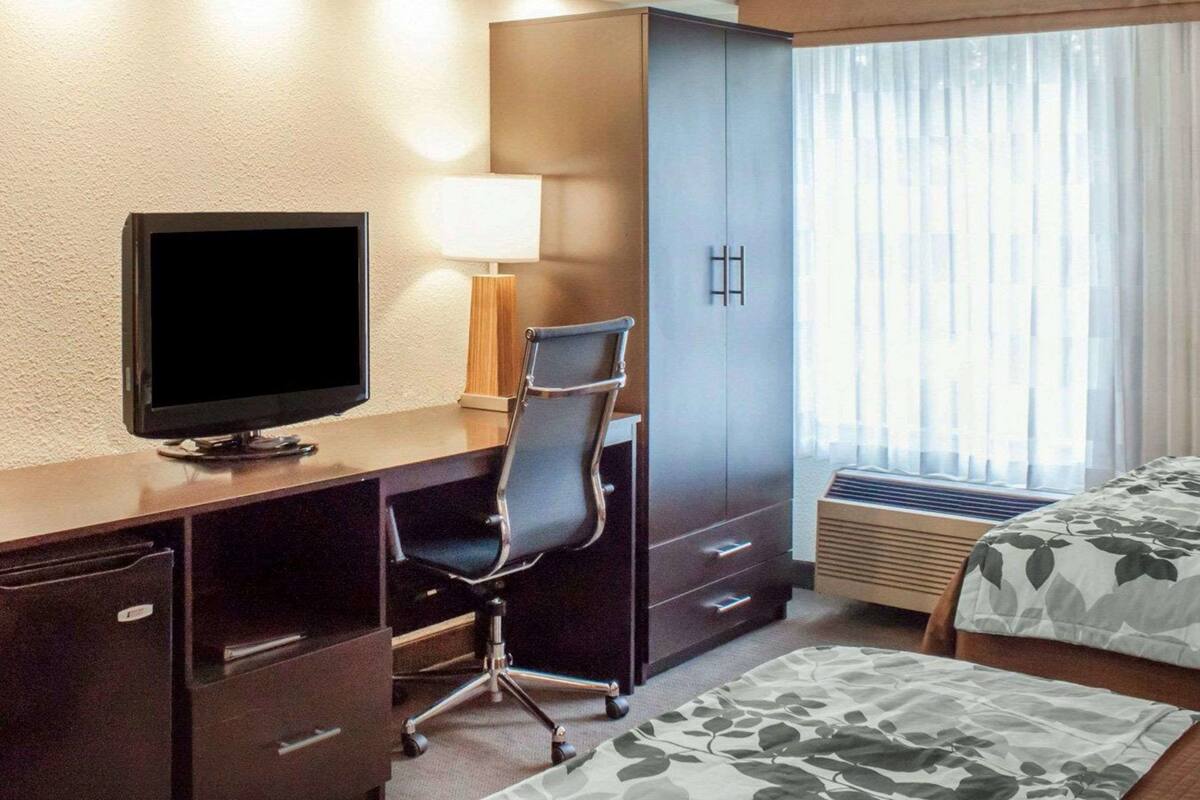 A hotel room with a desk, chair, television, wardrobe, and a bed.