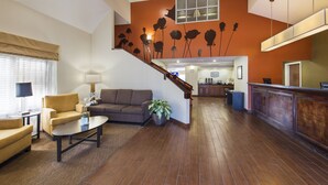 A spacious living area with a sofa, armchairs, a coffee table, and a potted plant. A staircase with a wooden railing leads to a kitchen area. - Sleep Inn North Charleston Ashley Phosphate (North Charleston)
