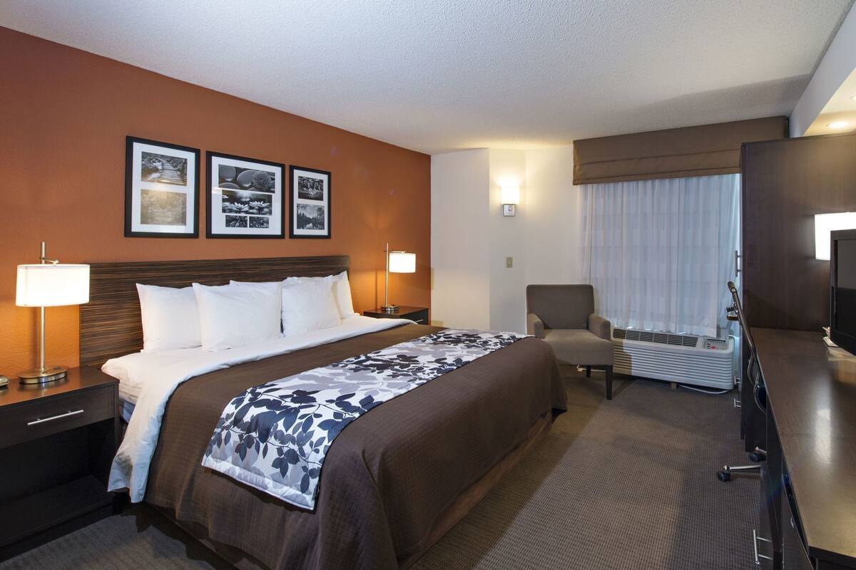 A hotel room with a bed, bedside tables, a desk with a TV, a chair, and a window with curtains.