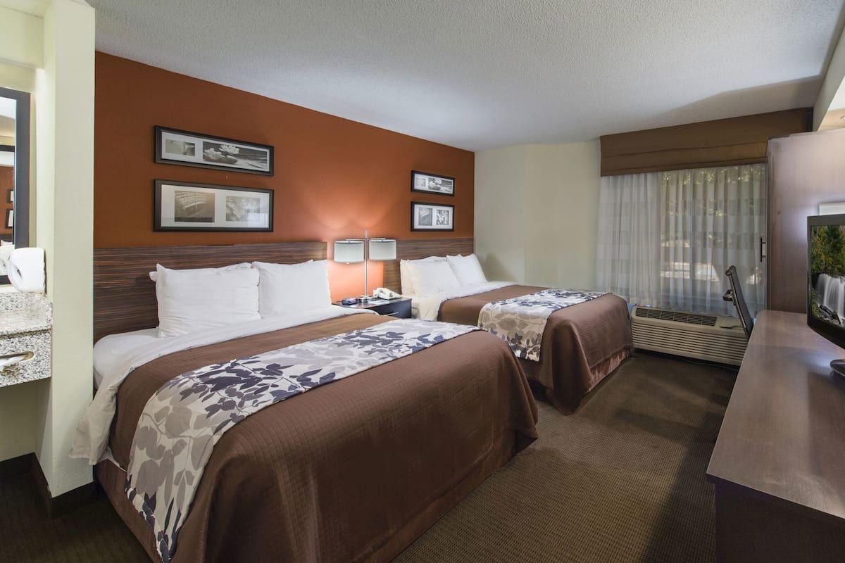 A hotel room with two beds, a desk, a television, and a window with curtains.