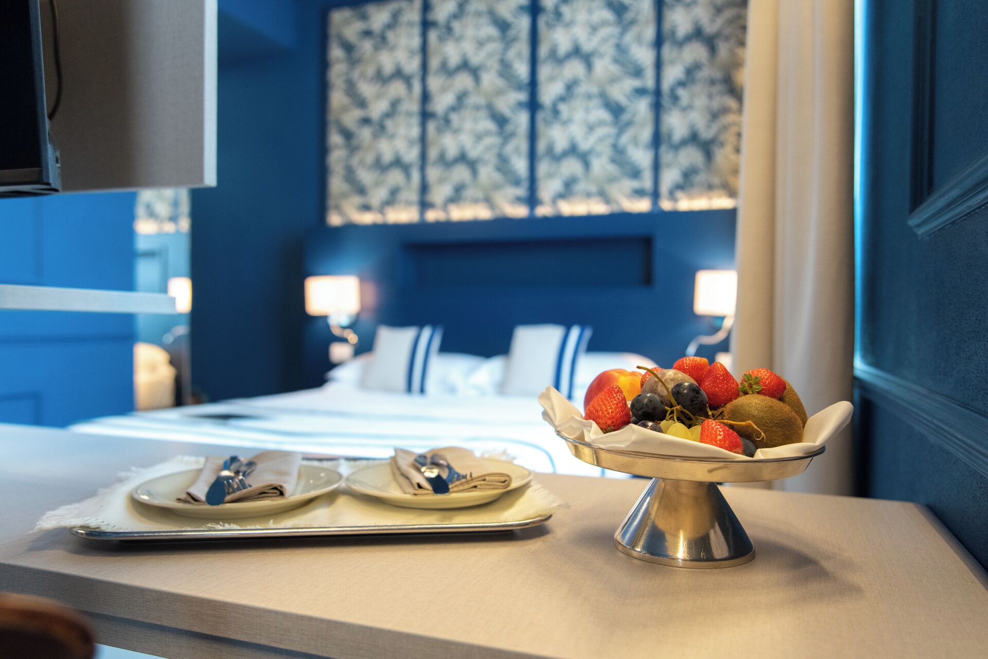 A hotel room with a bed, a bedside table with a fruit bowl, and a mirror.