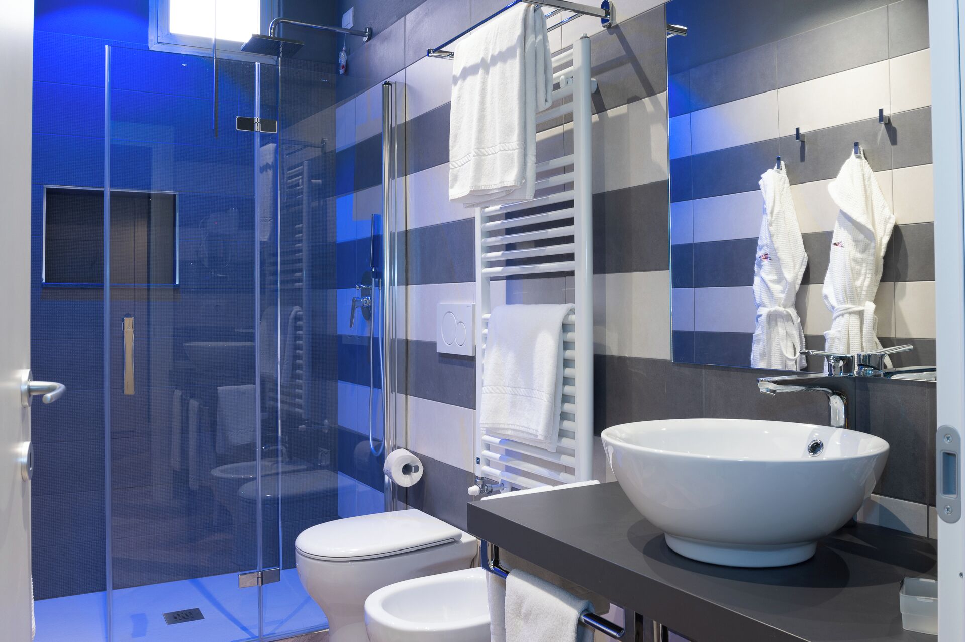 A modern bathroom with a glass shower enclosure, a white sink, and a towel rack.