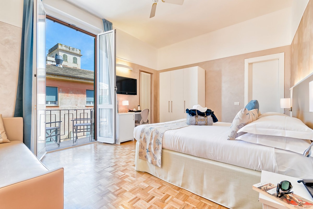 Moderni hotellihuone, jossa on sänky, työpöytä ja parveke, jolta on näkymä kaupunkiin.