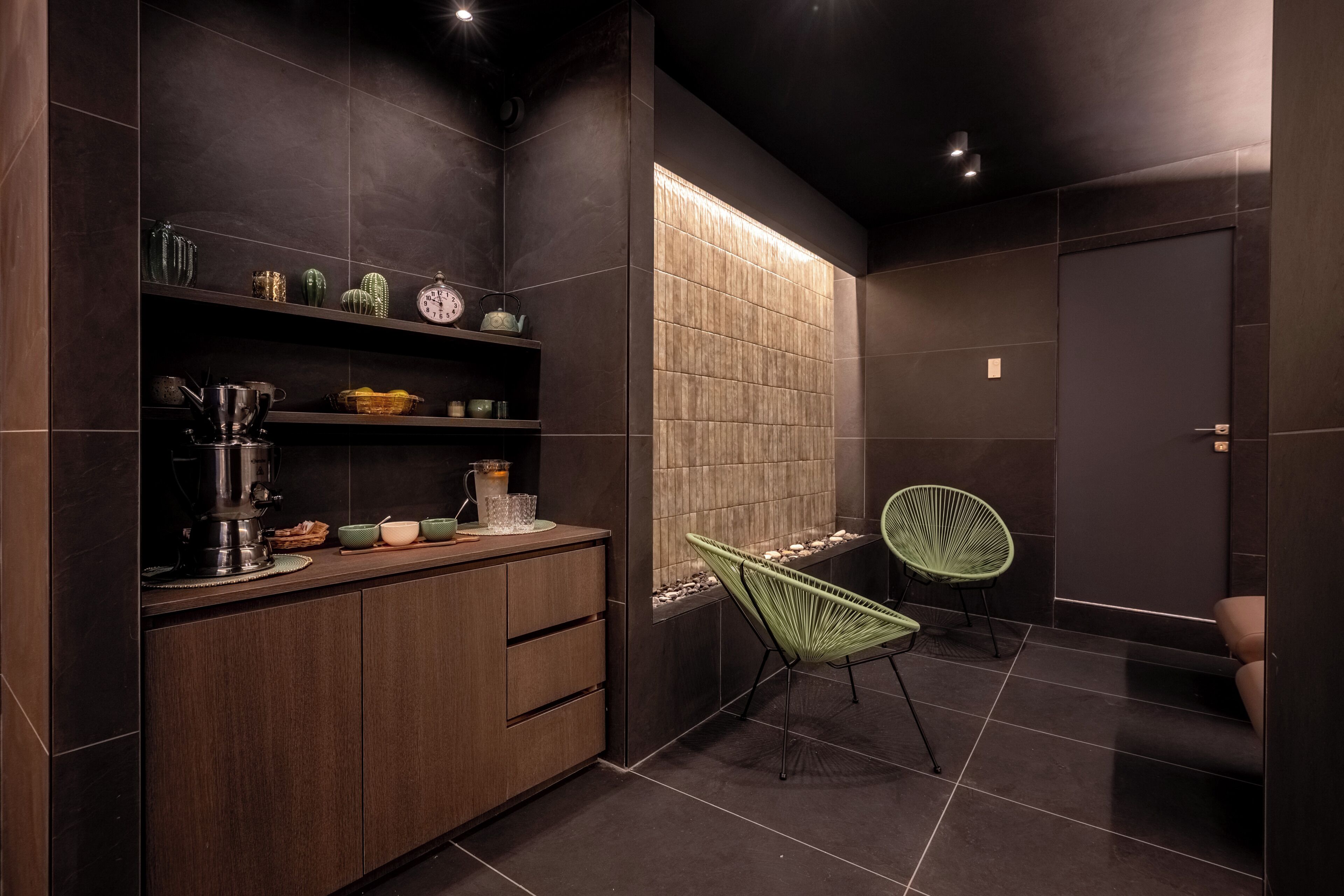 Una cocina moderna con baldosas oscuras, armarios de madera y una silla verde.