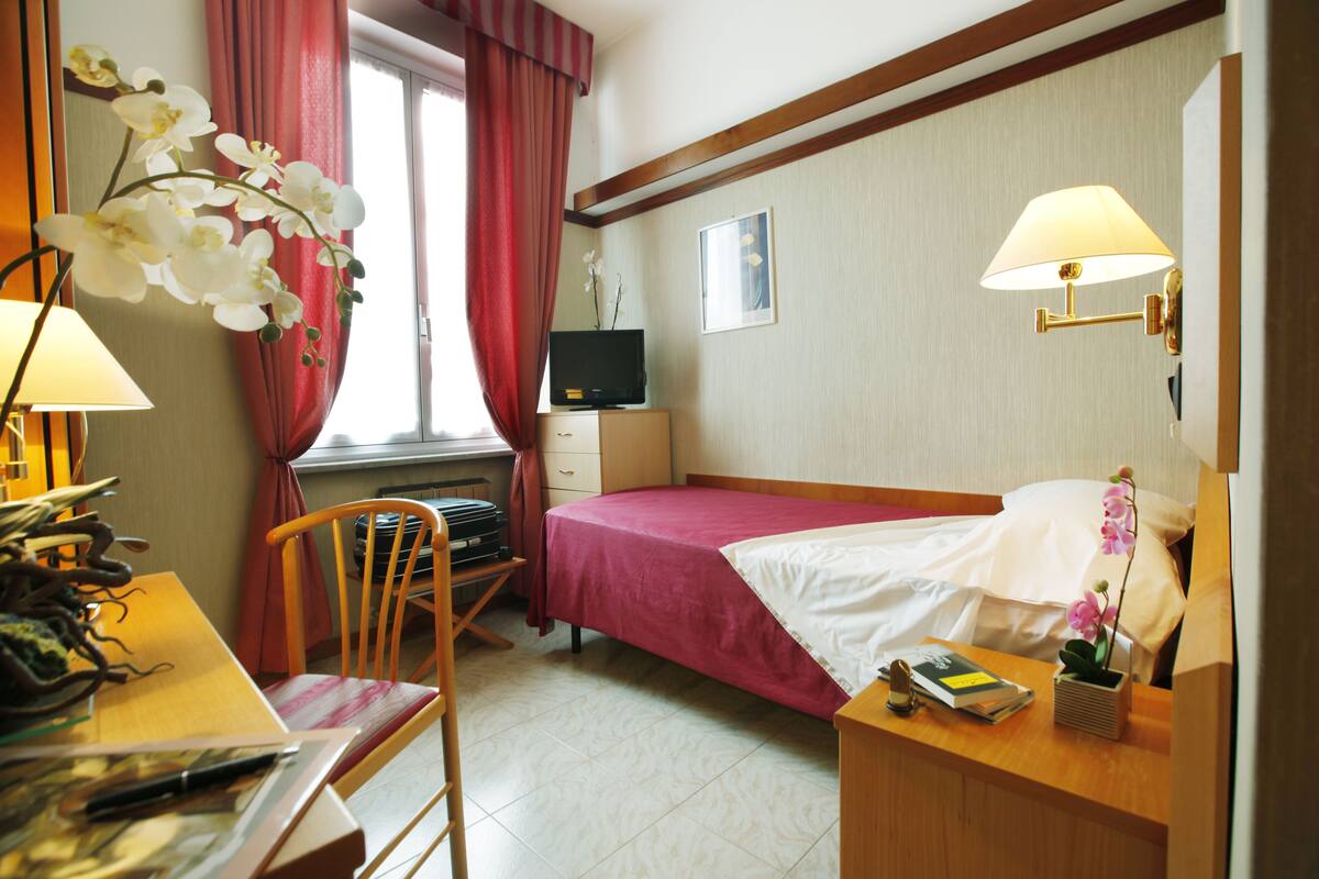A hotel room with a bed, desk, chair, TV, and lamps.