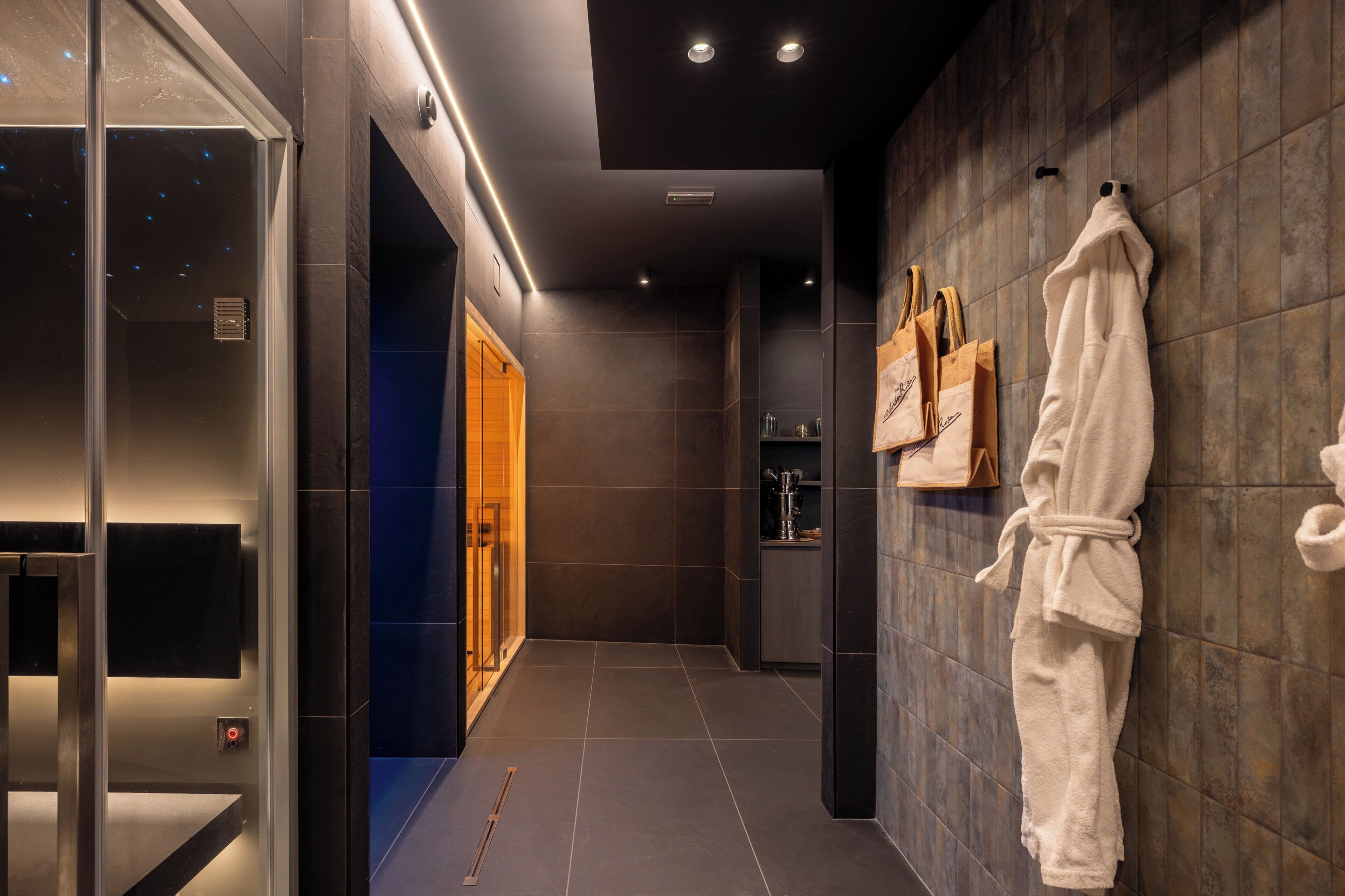 A modern bathroom with a glass shower enclosure, a robe hanging on the wall, and a towel rack.
