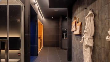 A modern bathroom with a glass shower enclosure, a robe hanging on the wall, and a towel rack.