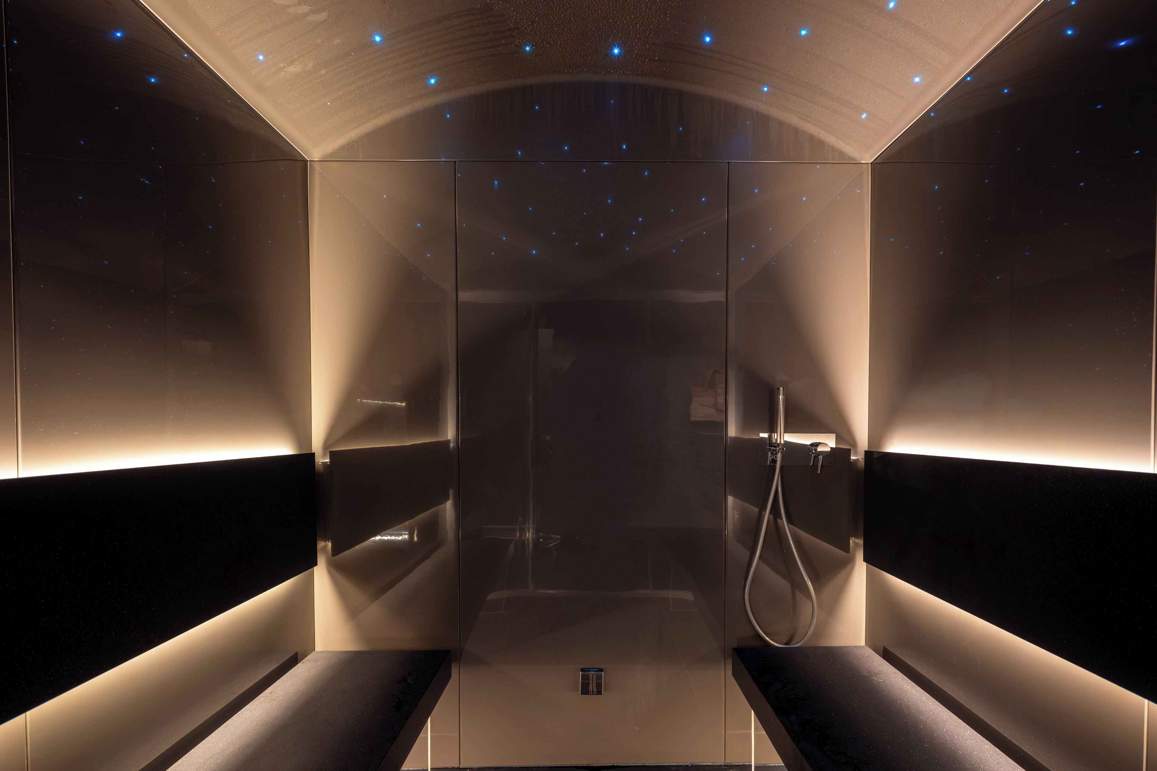 A modern, dimly lit room with a glass partition, a bench, and a shower area.