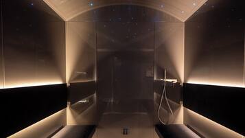 A modern, dimly lit room with a glass partition, a bench, and a shower area.