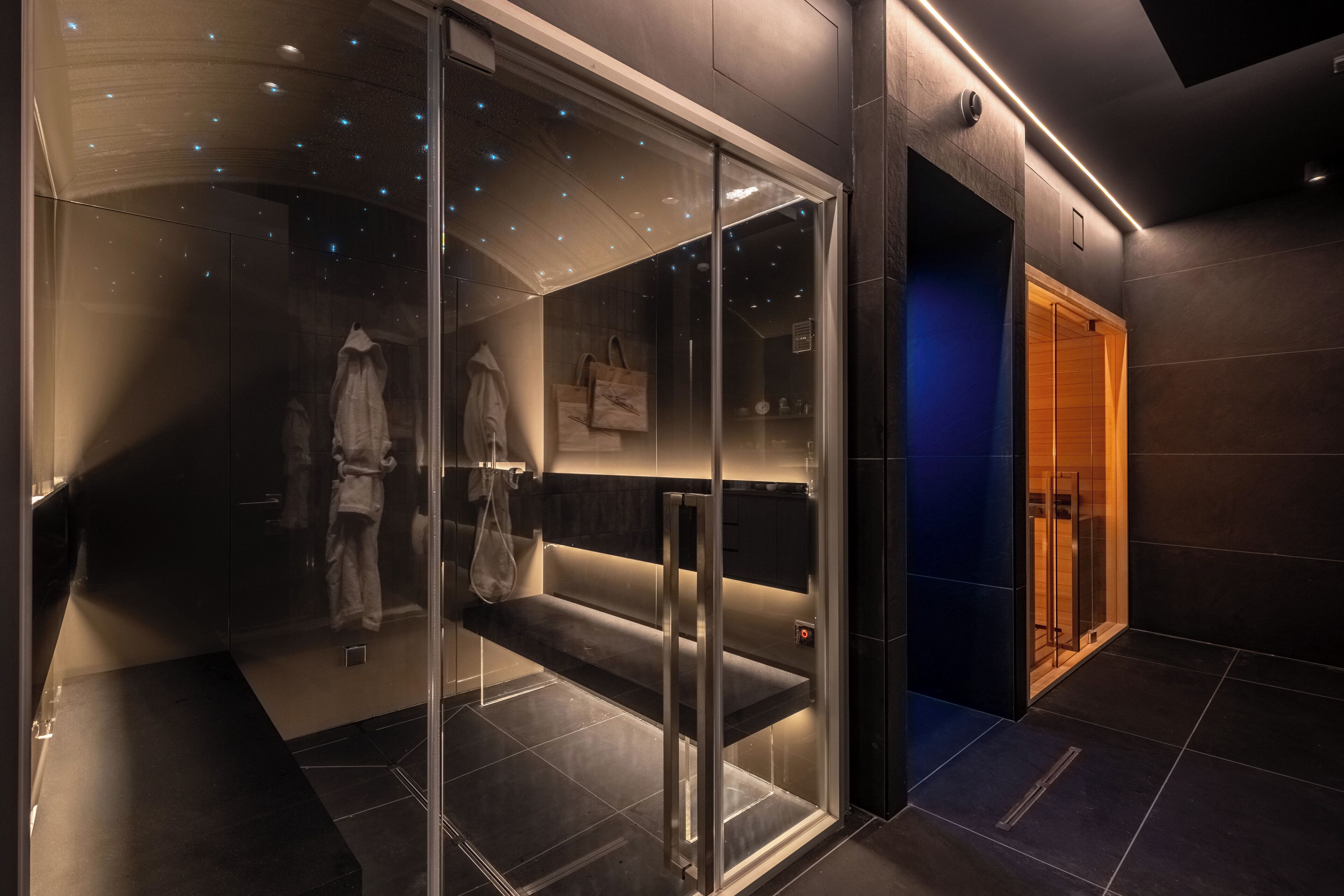 Una hall d'albergo moderna con un divisorio in vetro, ingresso illuminato di blu e l'ascensore ben visibile.