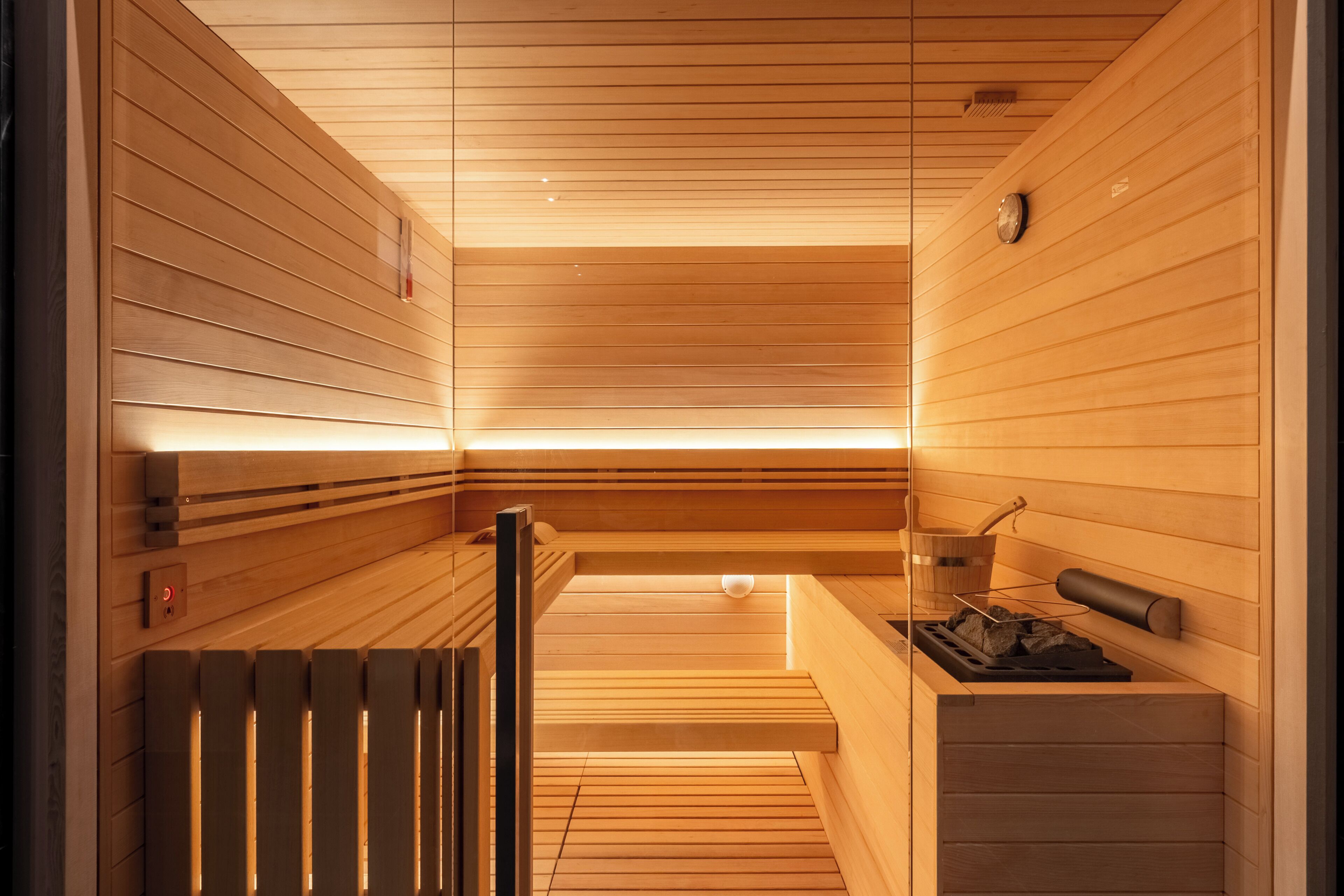 Un sauna avec des murs et des bancs en bois, un appareil de chauffage et un seau.