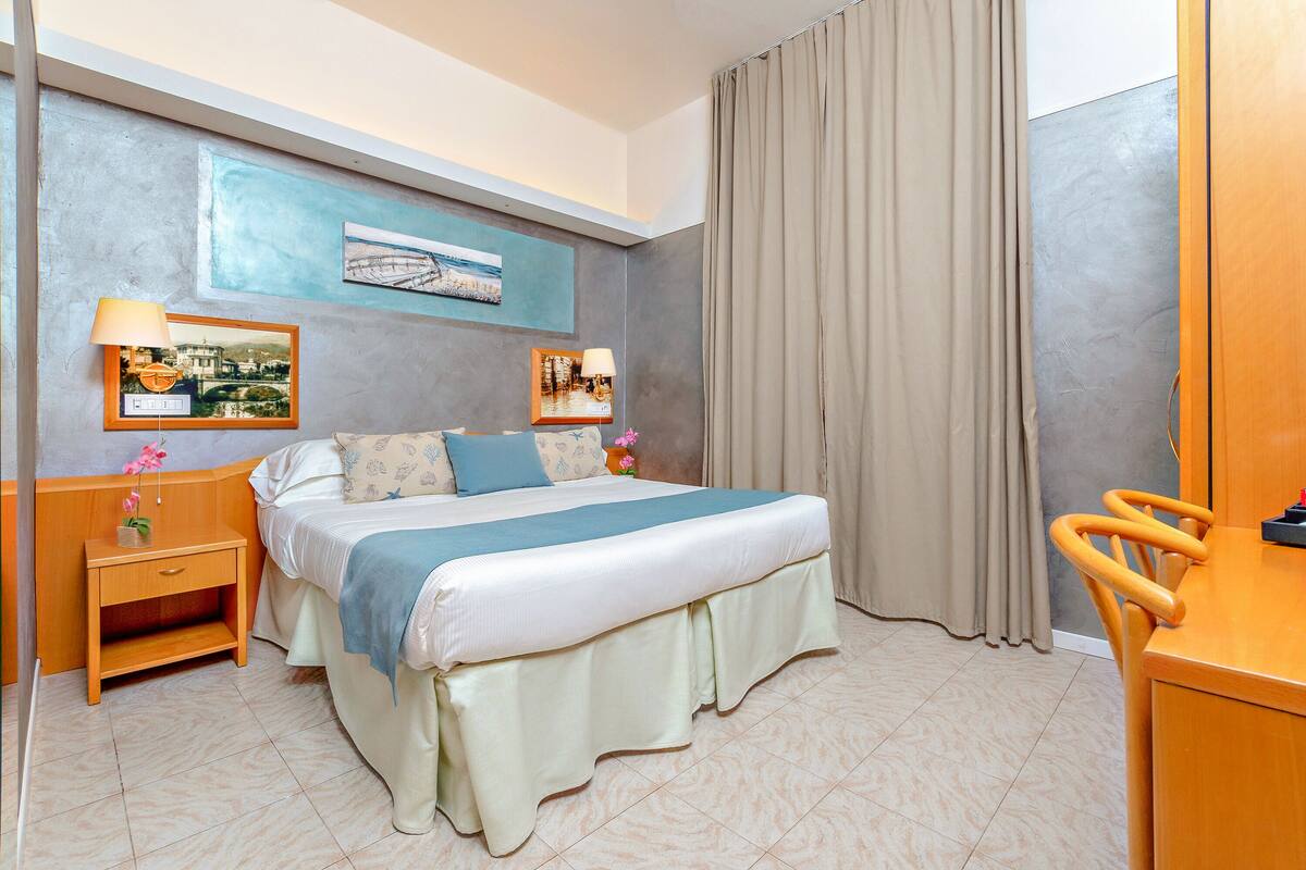 A hotel room with a bed, bedside tables, a desk, and a chair.