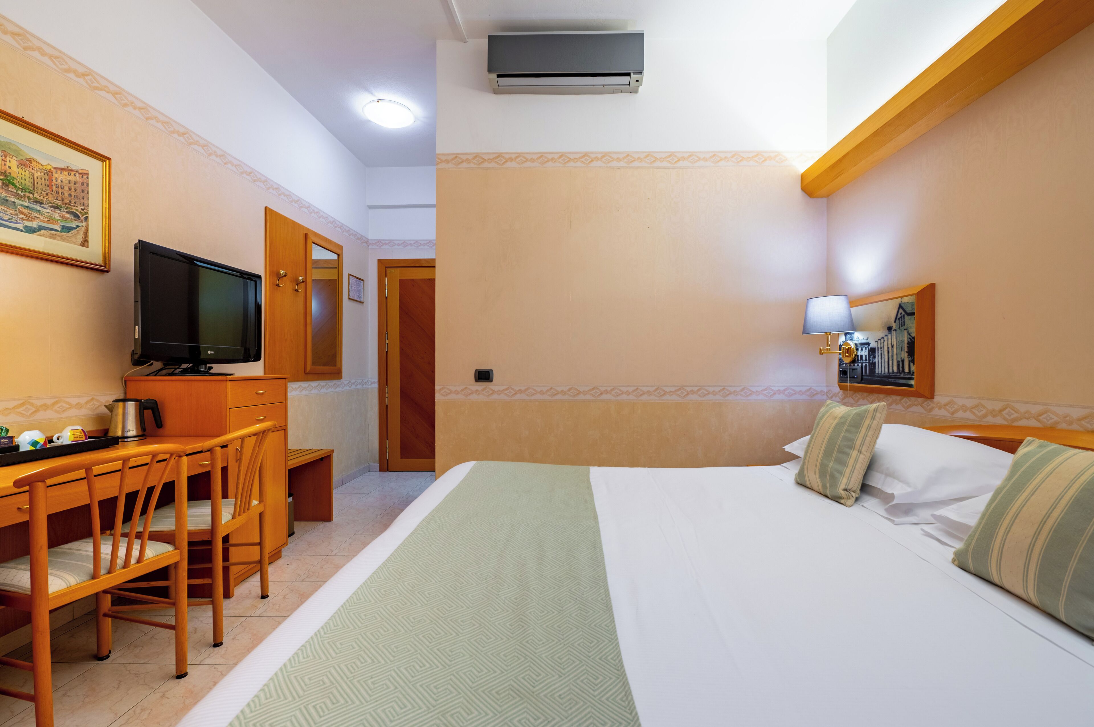 Una camera d'albergo con un letto, una scrivania con televisore, una macchina del caffè e una sedia.