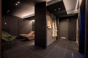 A modern bathroom with dark tiles, a green chair, a massage chair, and towels hanging on the wall. - Hotel Monte Rosa (Chiavari)