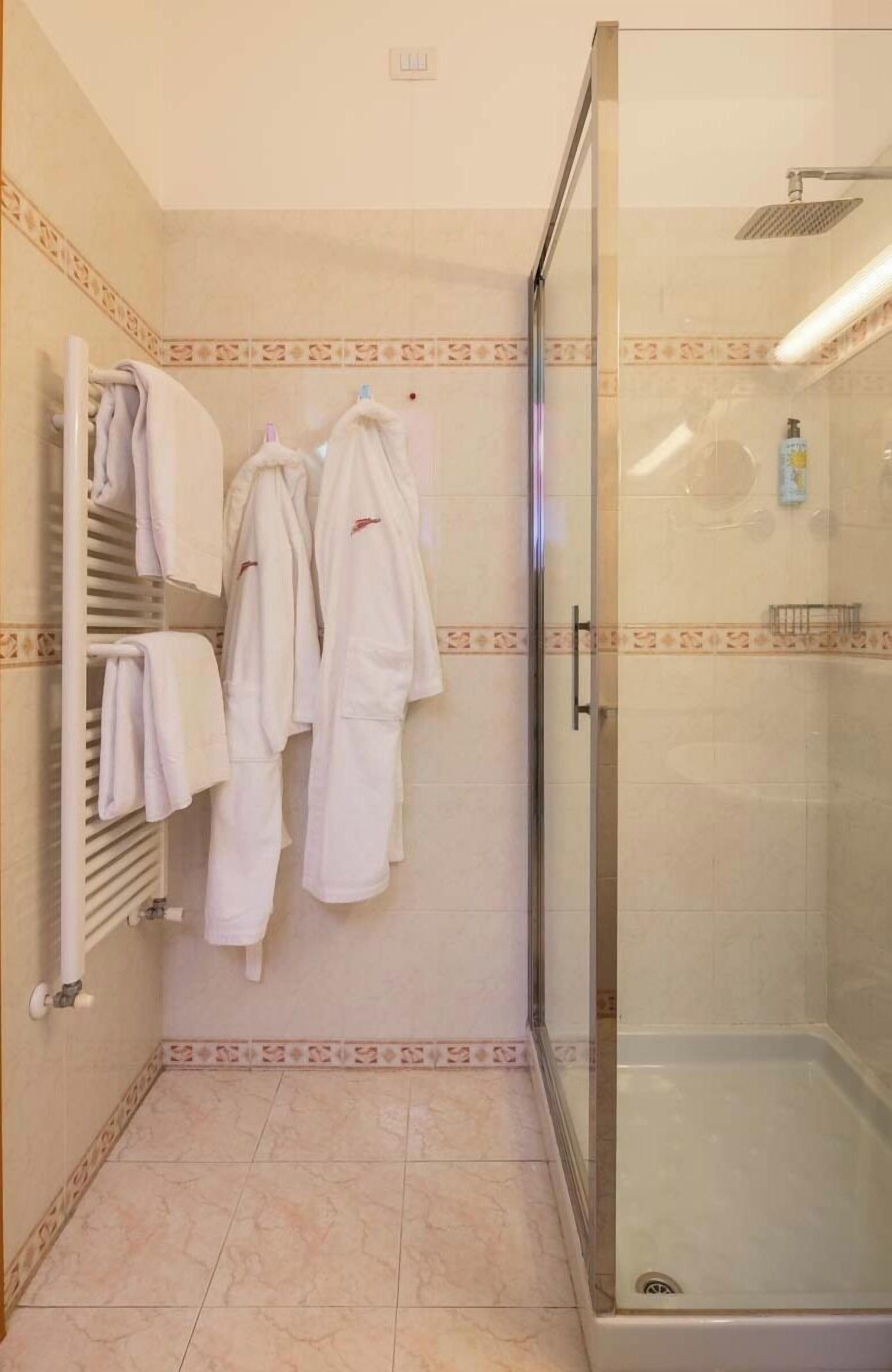 A bathroom with a glass-enclosed shower, a towel rack with multiple white towels, and patterned floor tiles.