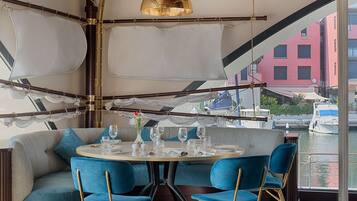 A dining area with a round table, blue chairs, and a view of boats through large windows.