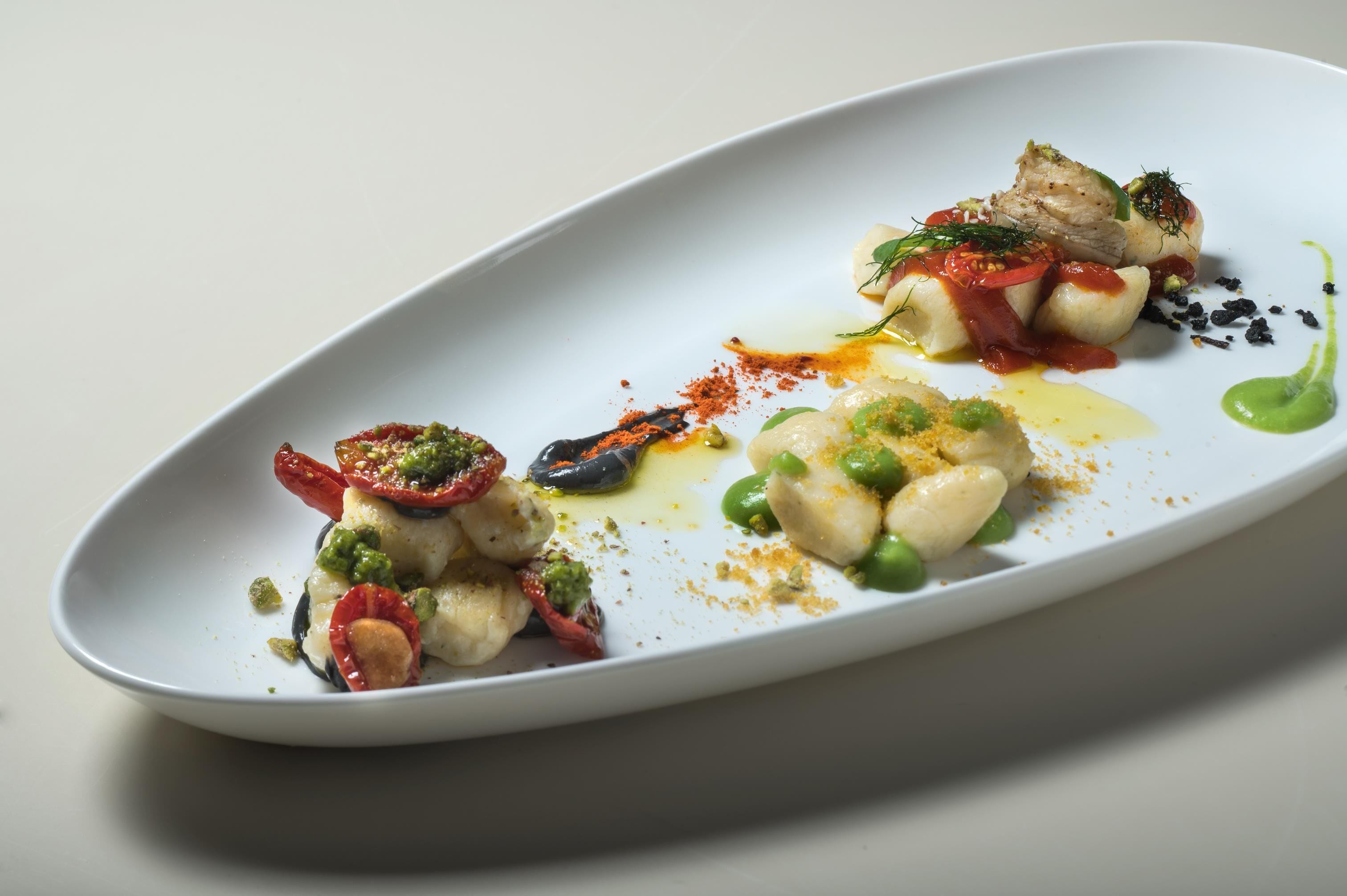 Een wit ovaal bord met een zeevruchtengerecht, inclusief garnalen, coquilles en een groene saus.
