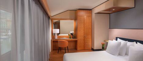A hotel room with a large bed, a desk with a chair, a wardrobe, and a window with curtains.